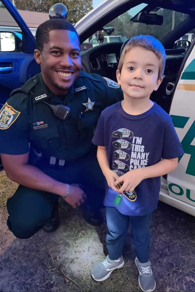 Sheriff and kid posing for picture in front of police car
