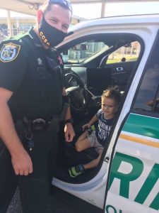 Deputy with a mask on showing a kid his car