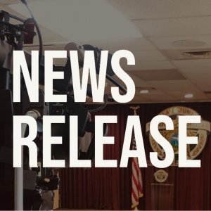 News release graphic, words against a darkened background with a camera looking at a podium